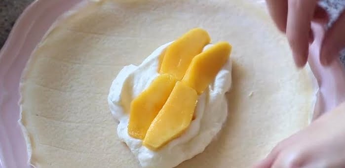 Để bột ra đĩa, phết kem sau đó đặt vài lát xoài chín lên trên